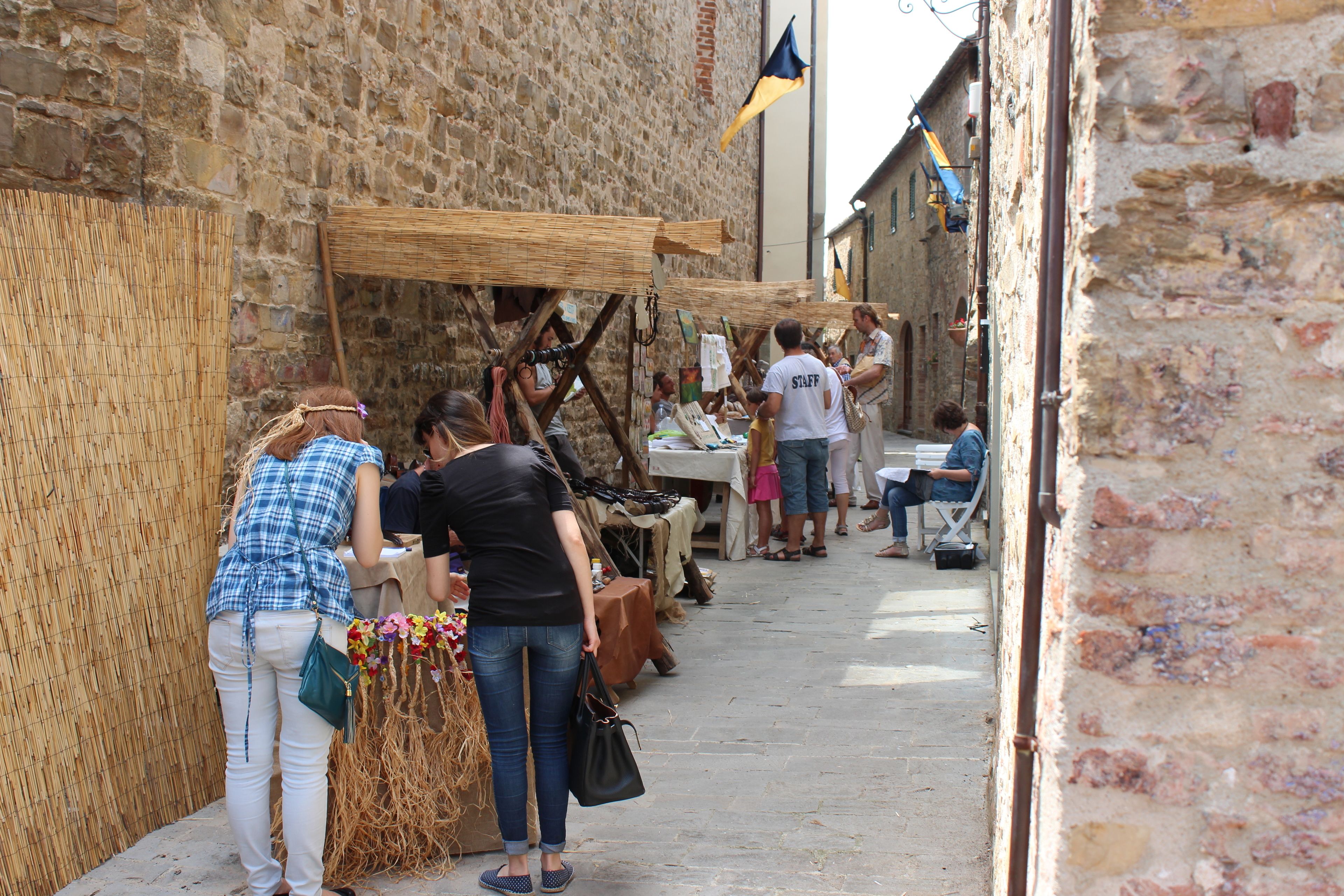 A narrow street with stone buildings, a market stall with goods, and people browsing.