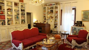 Un salón tradicional con un sofá rojo, una mesa de centro de madera y una estantería llena de objetos diversos.
