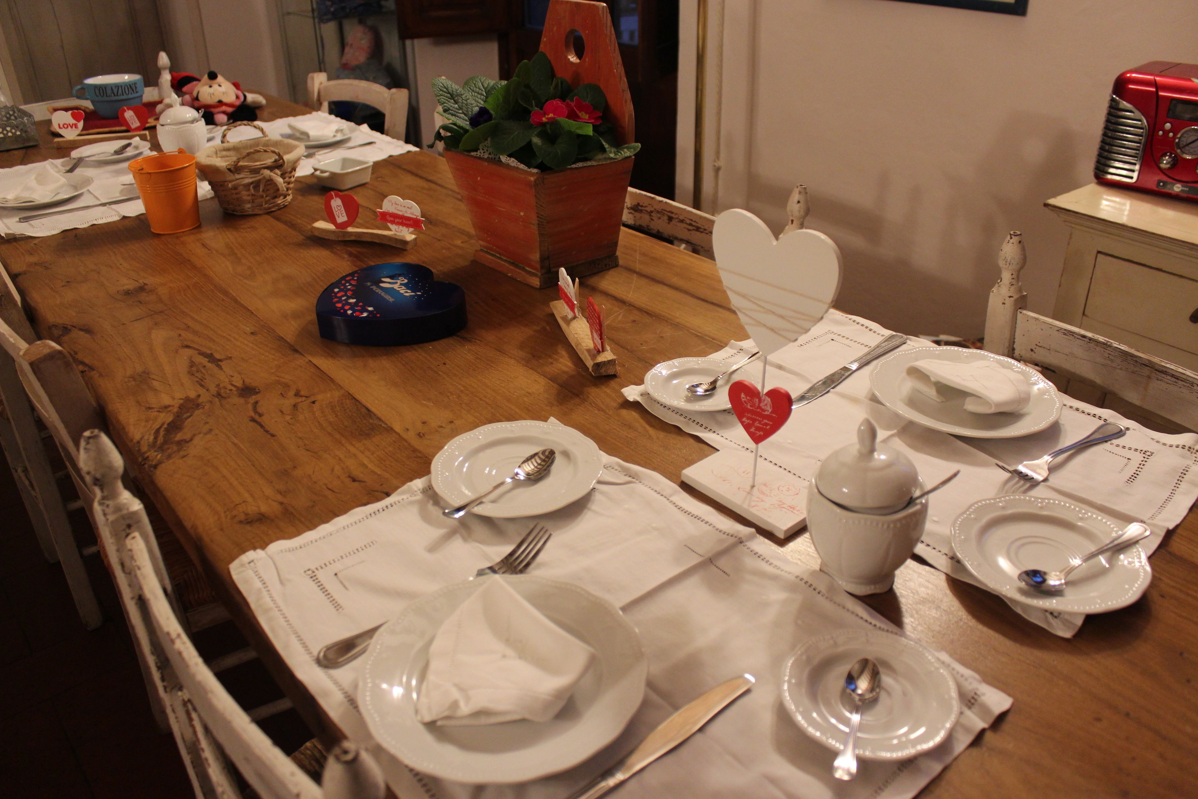 Een eettafel gedekt met witte borden, bestek en een hartvormig bordje.