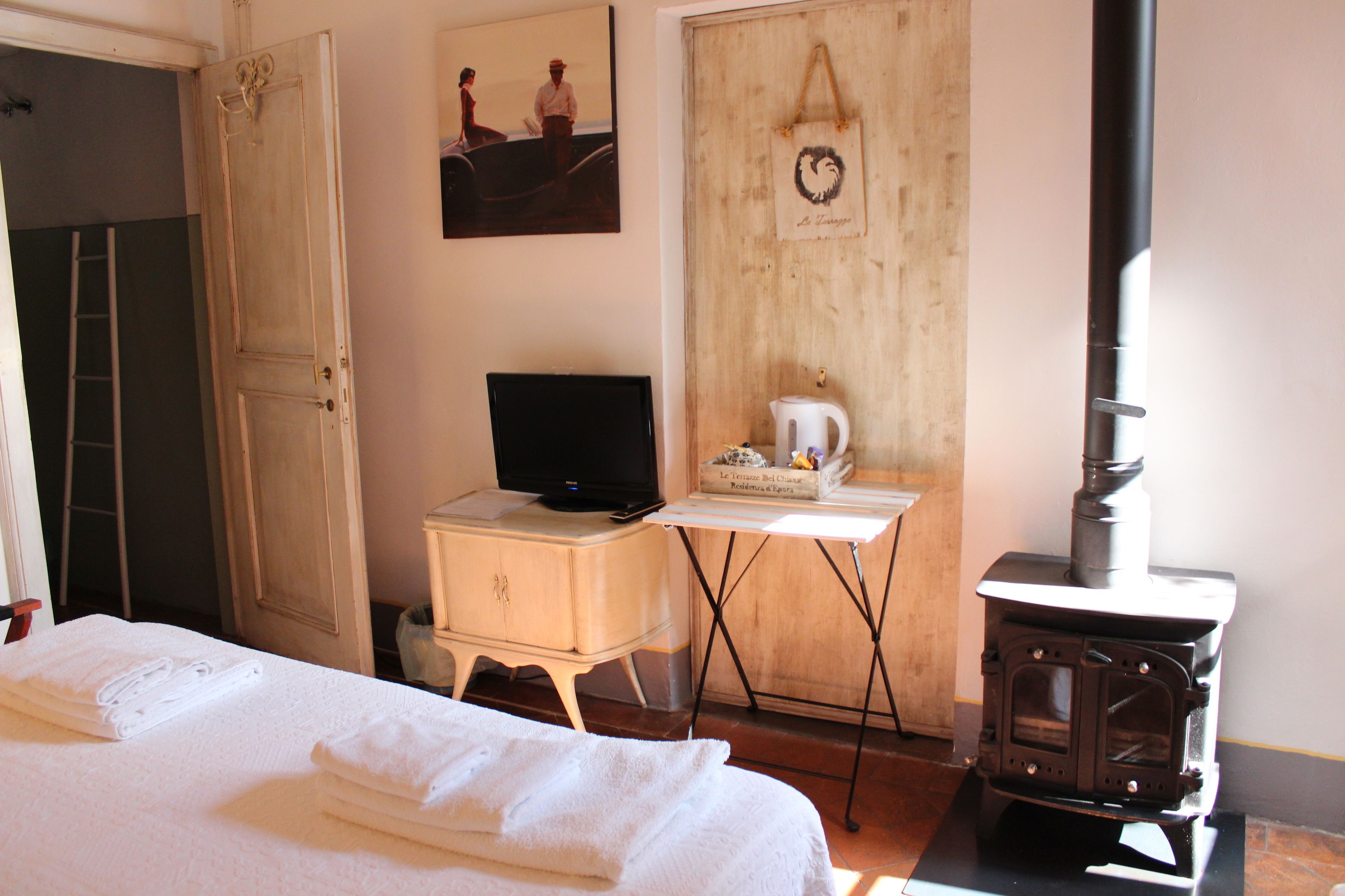 A room with a bed, a television, a wooden door, a white cabinet, and a wood-burning stove.