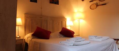 A neatly made bed with red pillows, a bedside table with a lamp, and a wall with sports equipment.