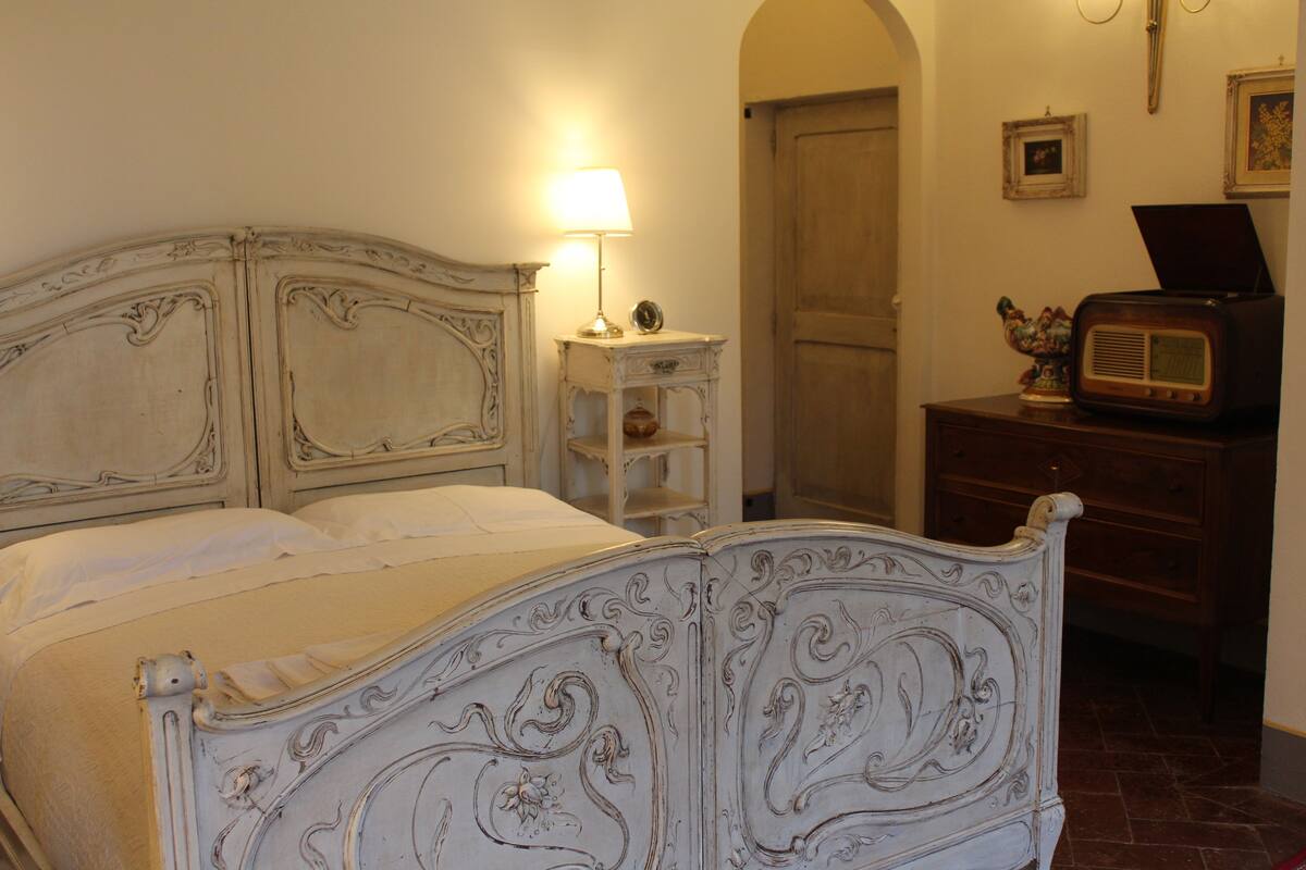 A bed with ornate headboard, a bedside lamp, and a dresser with a radio.