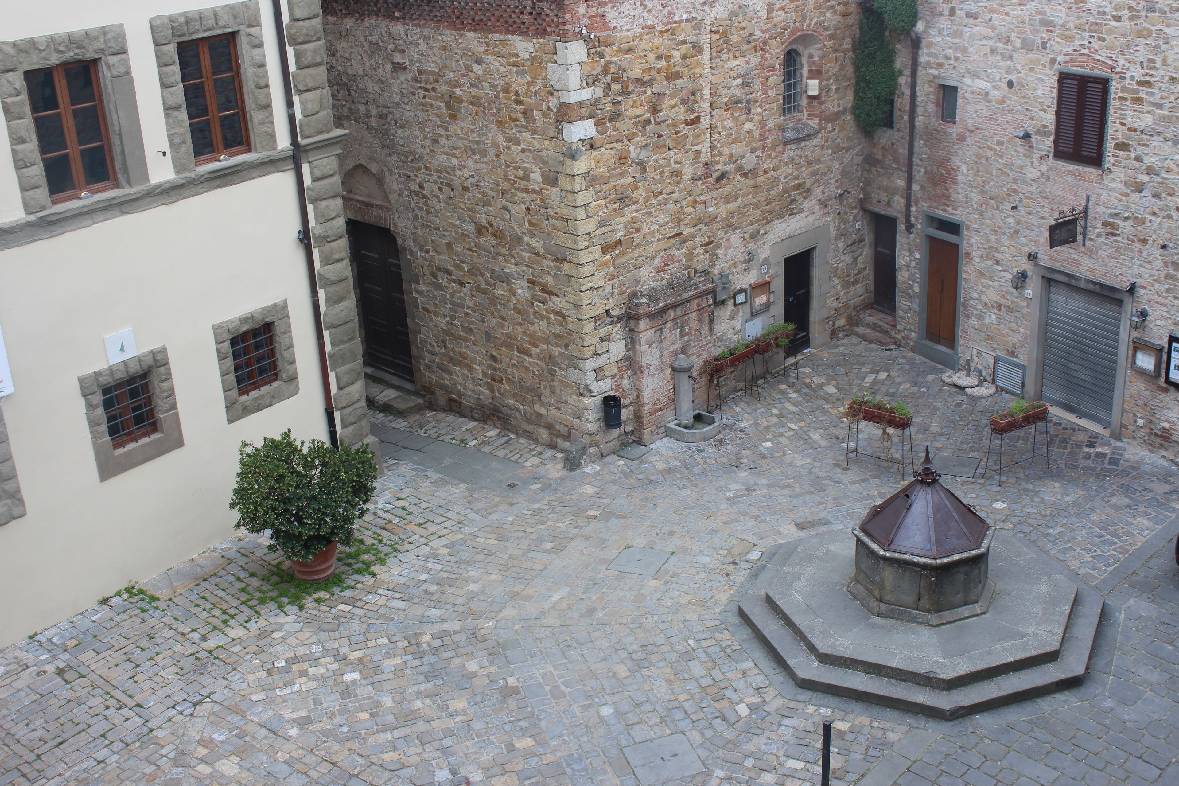 Un cortile in pietra con fontana, edifici in pietra e un piccolo giardino.