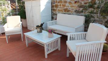 A white outdoor seating area with a table, chairs, and a potted plant.