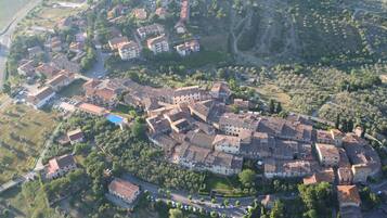 Una vista aerea di una città storica con una piazza centrale, circondata da edifici con tetti in tegole rosse, strette vie e aree verdi.