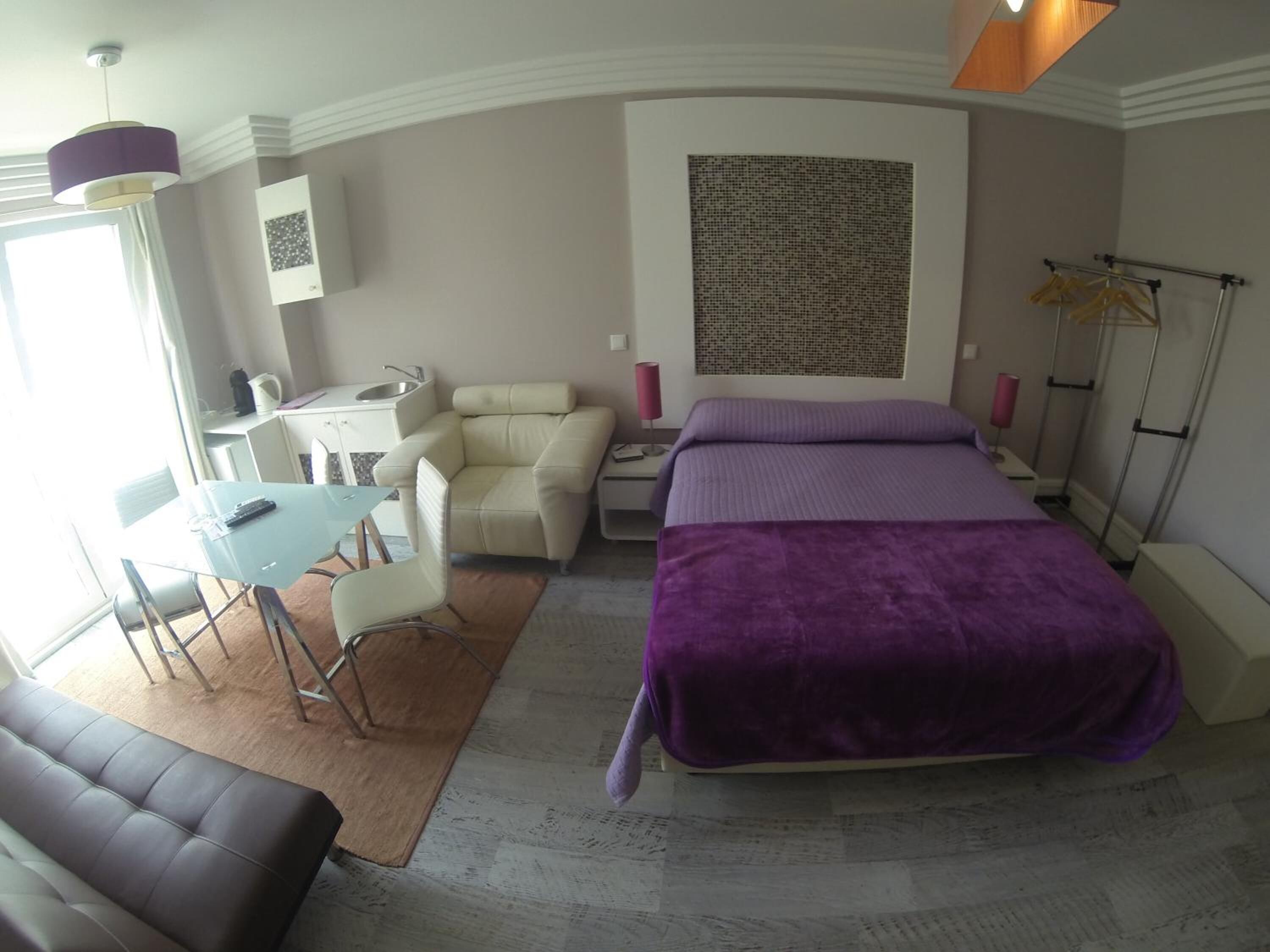A modern hotel room with a bed, a desk, a chair, and a sofa.