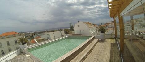 A rooftop swimming pool with wooden decking and a view of the cityscape.