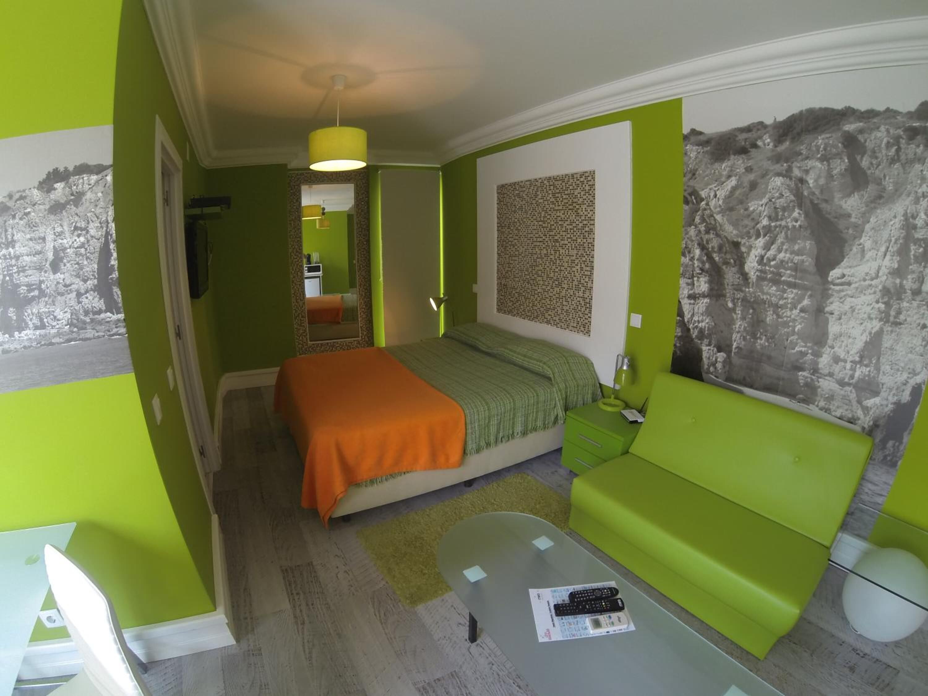 A compact hotel room with a bed, a green sofa, a small table, and a wall with a rock-like pattern.