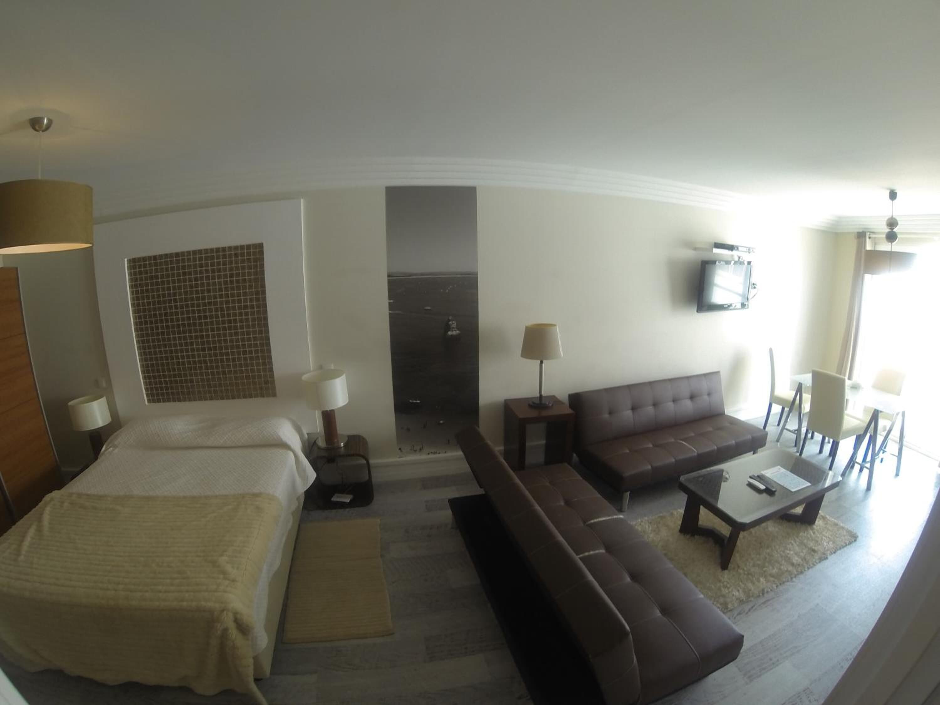 Une chambre d’hôtel avec un lit, un canapé, une table basse, une télévision et une vue sur la mer.