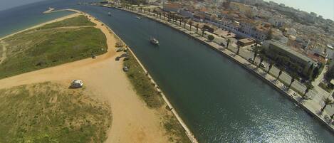 An aerial view of a coastal city with a river running through it, lined with buildings and a sandy beach.