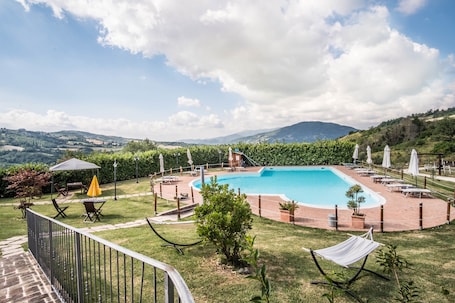 Una piscina al aire libre, sombrillas, sillones reclinables de piscina