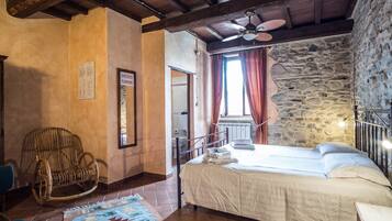 Un dormitorio con una cama, una silla de mimbre, una pared de piedra y un ventilador de techo.