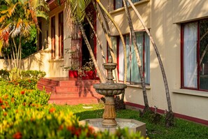 A garden with a fountain, palm trees, and a building with red accents.