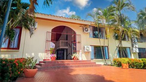 Un edificio de dos pisos con una entrada central, varios equipos de aire acondicionado y una variedad de plantas en macetas.