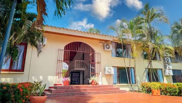 A two-story building with a central entrance, multiple air conditioning units, and a variety of potted plants.