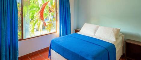 Un dormitorio con cama, cortinas y ventana con vistas a palmeras.