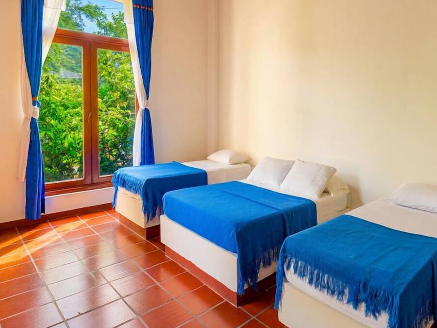 A hotel room with two beds, a window with curtains, and a tiled floor.