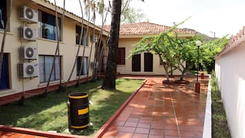 A courtyard with a tiled pathway, air conditioning units, and a tree.