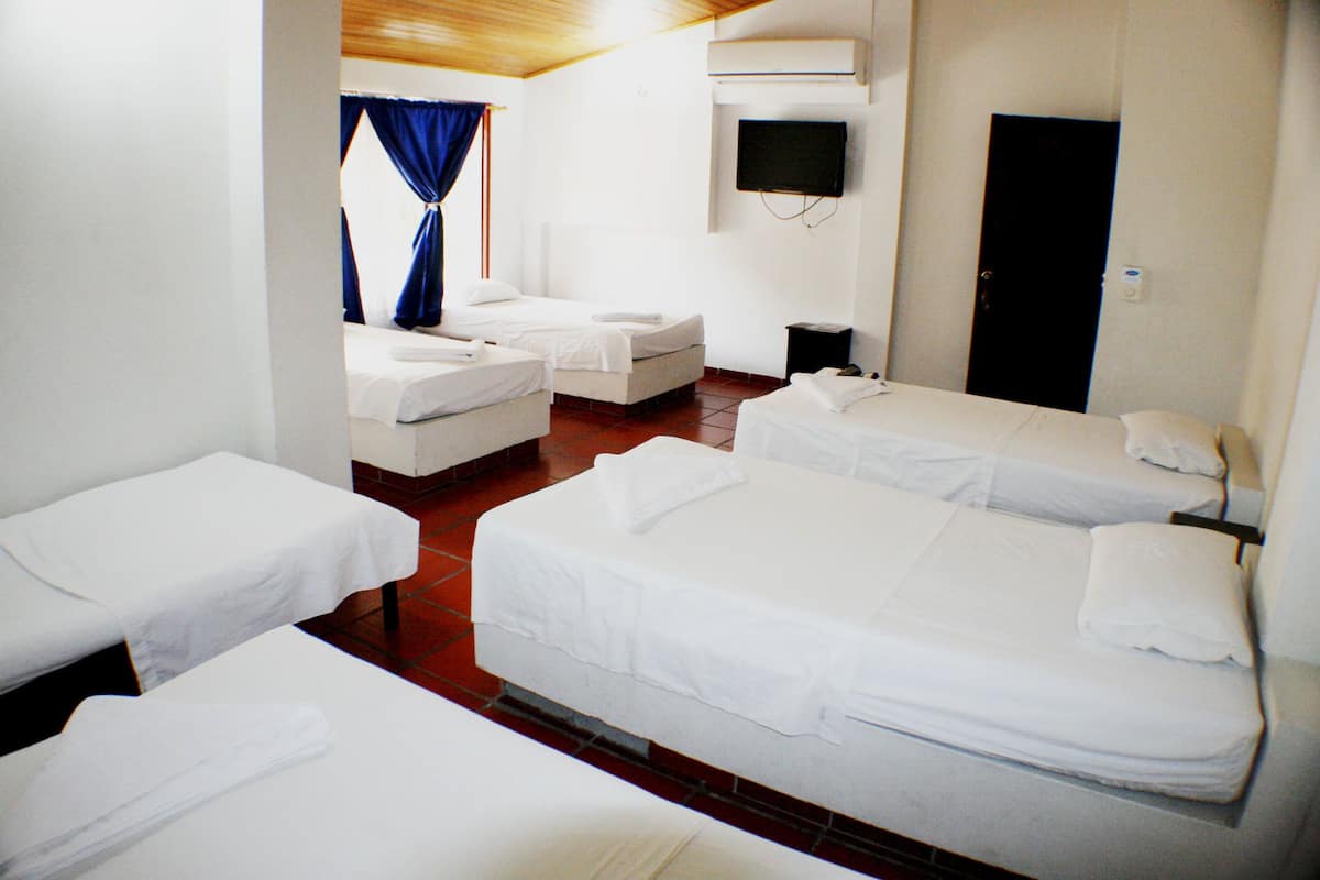 A hotel room with four single beds, a TV mounted on the wall, and a door to the right.