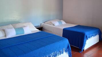 Une chambre avec deux lits, chacun recouvert d’une couverture bleue et agrémenté d’oreillers blancs. Les murs de la chambre sont blancs et le plafond est en bois.