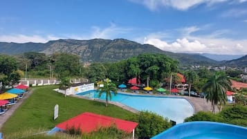 Un resort con piscina, mobiliario exterior y montañas al fondo.