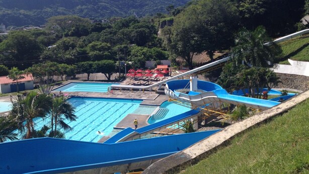 A swimming pool with a water slide, surrounded by palm trees and a mountainous backdrop. - Hotel y Parque Acuatico Agua Sol Alegría (Honda)
