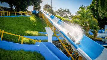 Un tobogán de agua con diseño azul y blanco, rodeado de césped y árboles.