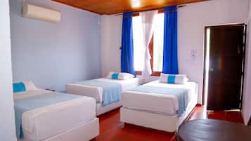 Una habitación de hotel con dos camas individuales, una mesita pequeña, un ventilador de techo y una ventana con cortinas.