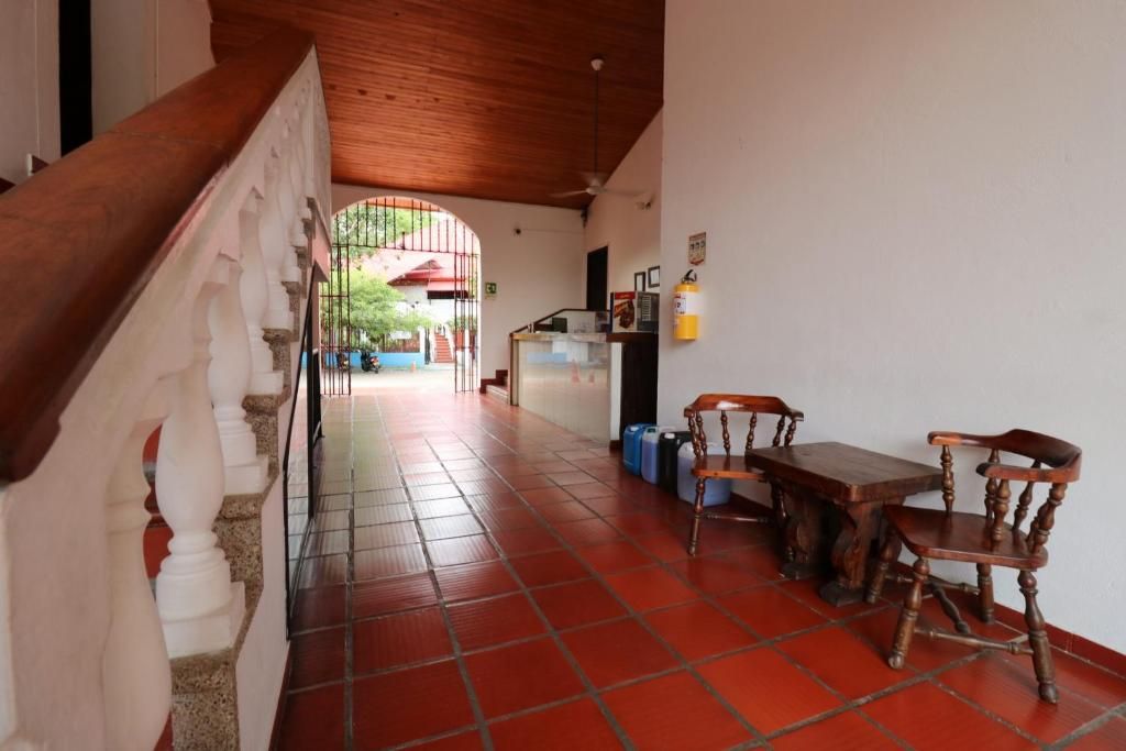 A hallway with a staircase, a dining area with wooden furniture, and a view of a red-roofed building through an archway.