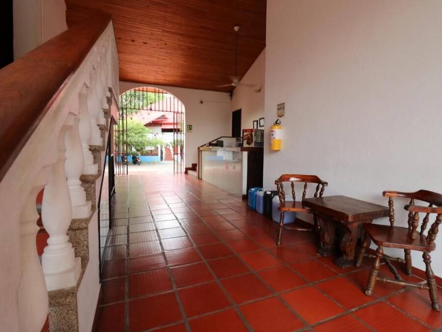 A hallway with a staircase, a dining area with wooden furniture, and a view of a red-roofed building through an archway.