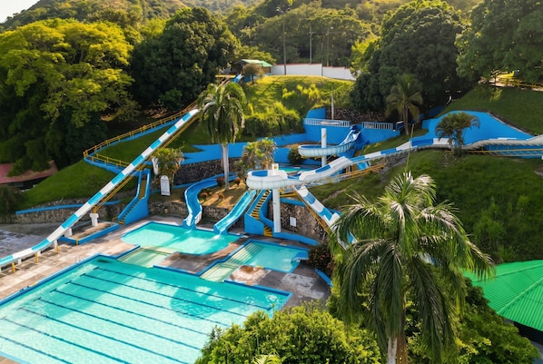 Parque acuático con múltiples toboganes y piscinas, rodeado de exuberante vegetación.