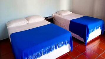Duas camas de solteiro com lençóis brancos e colchas azuis em um quarto com piso de ladrilho vermelho.