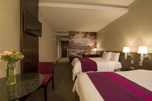 A hotel room with a bed, bedside lamps, a desk with a vase of flowers, and a wall with a scenic poster. - Arawi Miraflores Prime (Lima)