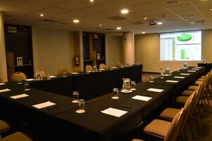 Un salón de conferencias con una larga mesa, sillas, una pantalla de proyector y una presentación en la pared.