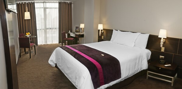 A hotel room with a large bed, a desk with a chair, a small table with a chair, and two bedside lamps. - Arawi Miraflores Prime (Lima)