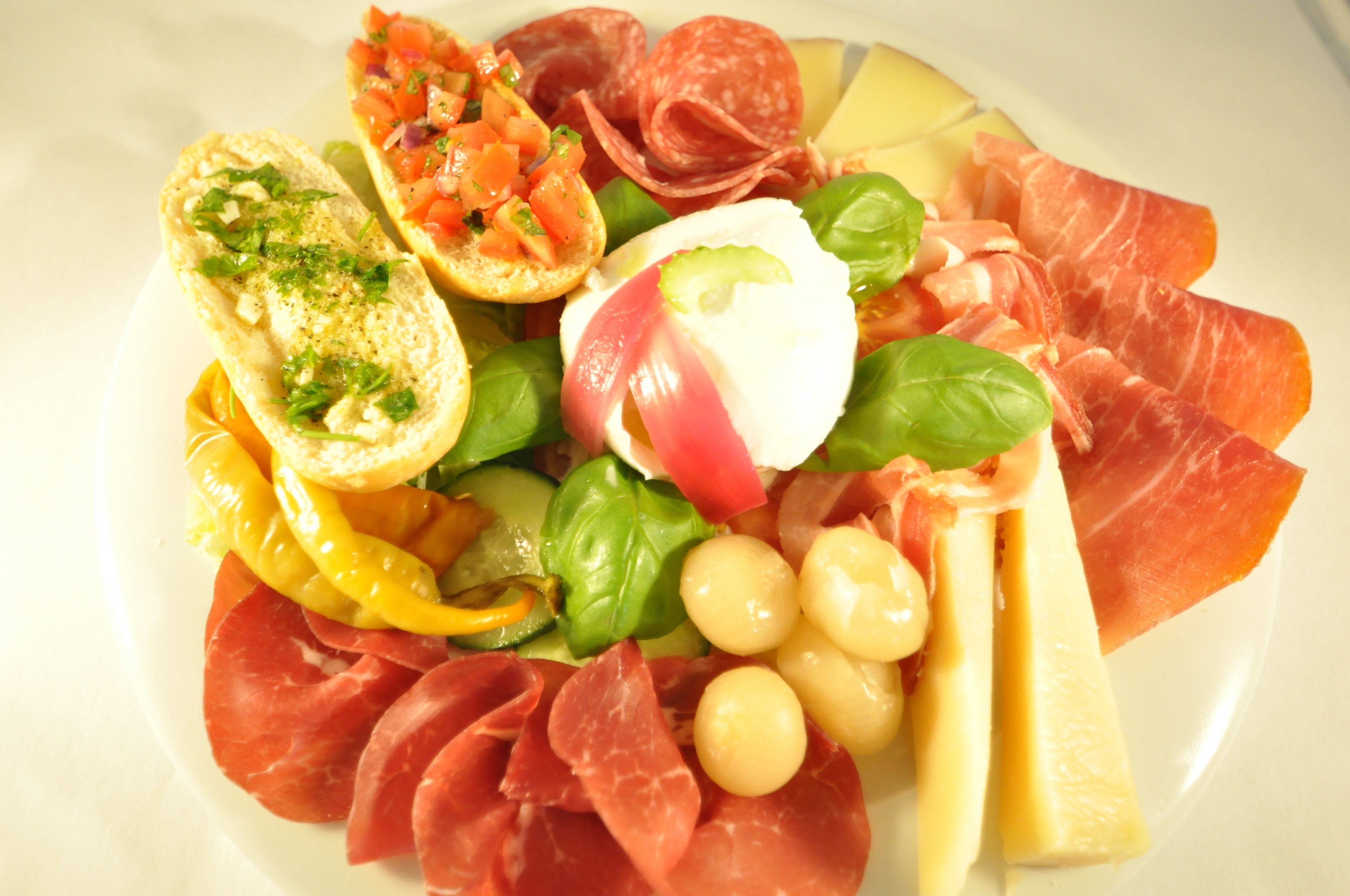 A plate of assorted food including bread, cheese, tomatoes, basil, and various meats.