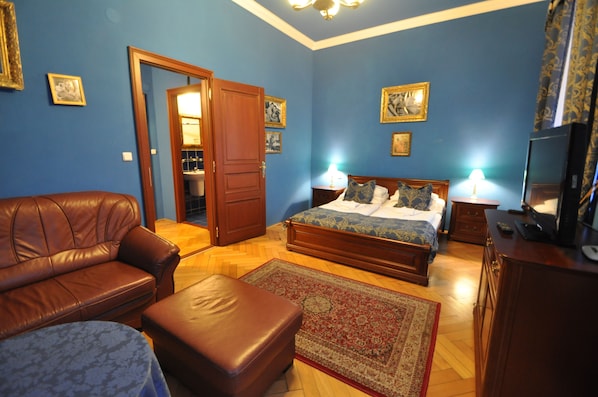 A bedroom with a bed, a brown leather sofa, a wooden dresser, and a nightstand with a lamp. - Grand Hotel Praha (Jicin)