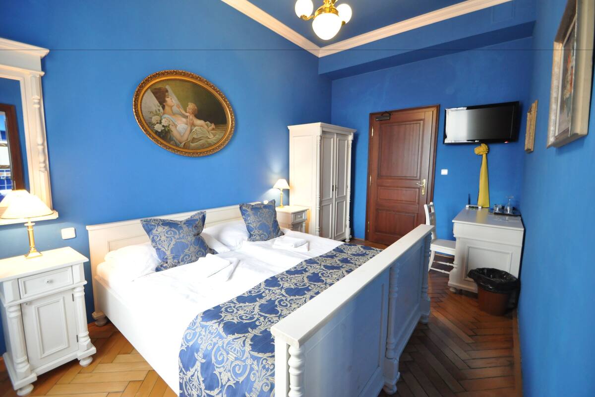A bedroom with a large bed, a painting on the wall, a television, and a cabinet.