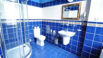 A bathroom with blue tiles, a glass shower enclosure, a toilet, a sink, and a mirror with a decorative frame.