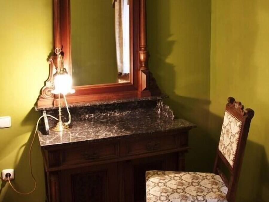 Un baño con tocador de madera, espejo, silla y alfombra estampada.