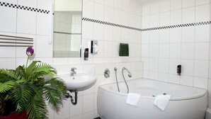 Un bagno moderno con piastrelle bianche, una vasca da bagno ampia, un lavandino, uno specchio e una pianta in vaso.