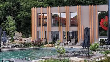 A modern building with vertical wooden slats, a swimming pool, and outdoor seating.