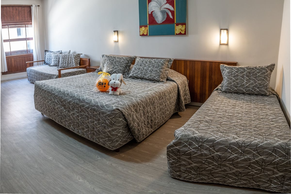 A hotel room with two beds, a wooden headboard, a wall-mounted painting, and a window with curtains.