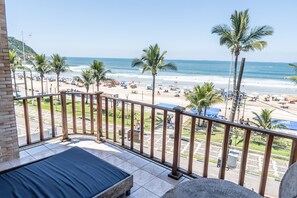 A balcony with a view of a beach, palm trees, and a clear sky. - Strand Hotel (Guarujá)