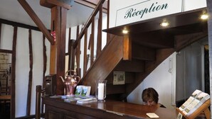 A reception desk with a sign reading "Reception" in a building with exposed wooden beams and a staircase. - Auberge du Gros Tilleul (Argoules)