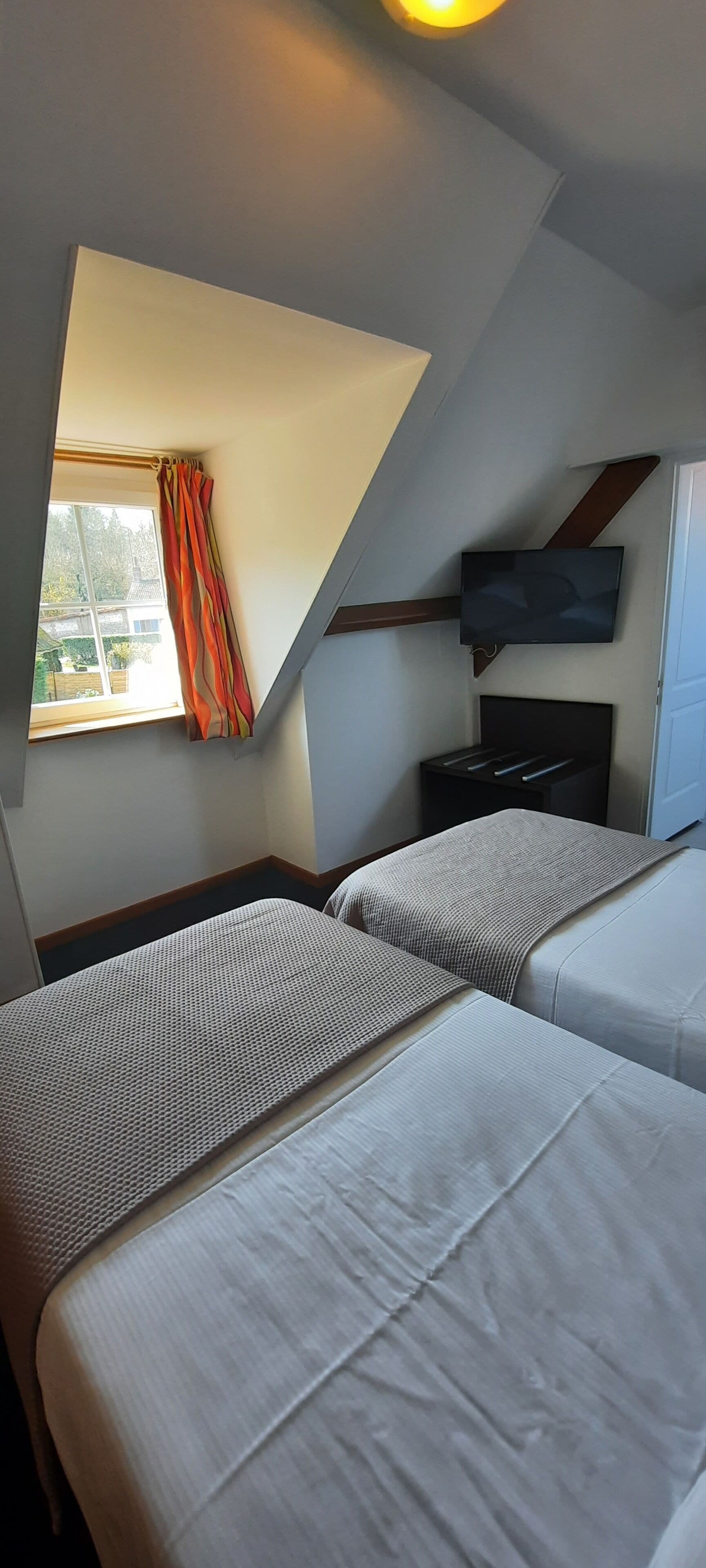 A room with two beds, a TV mounted on the wall, and a window with curtains.