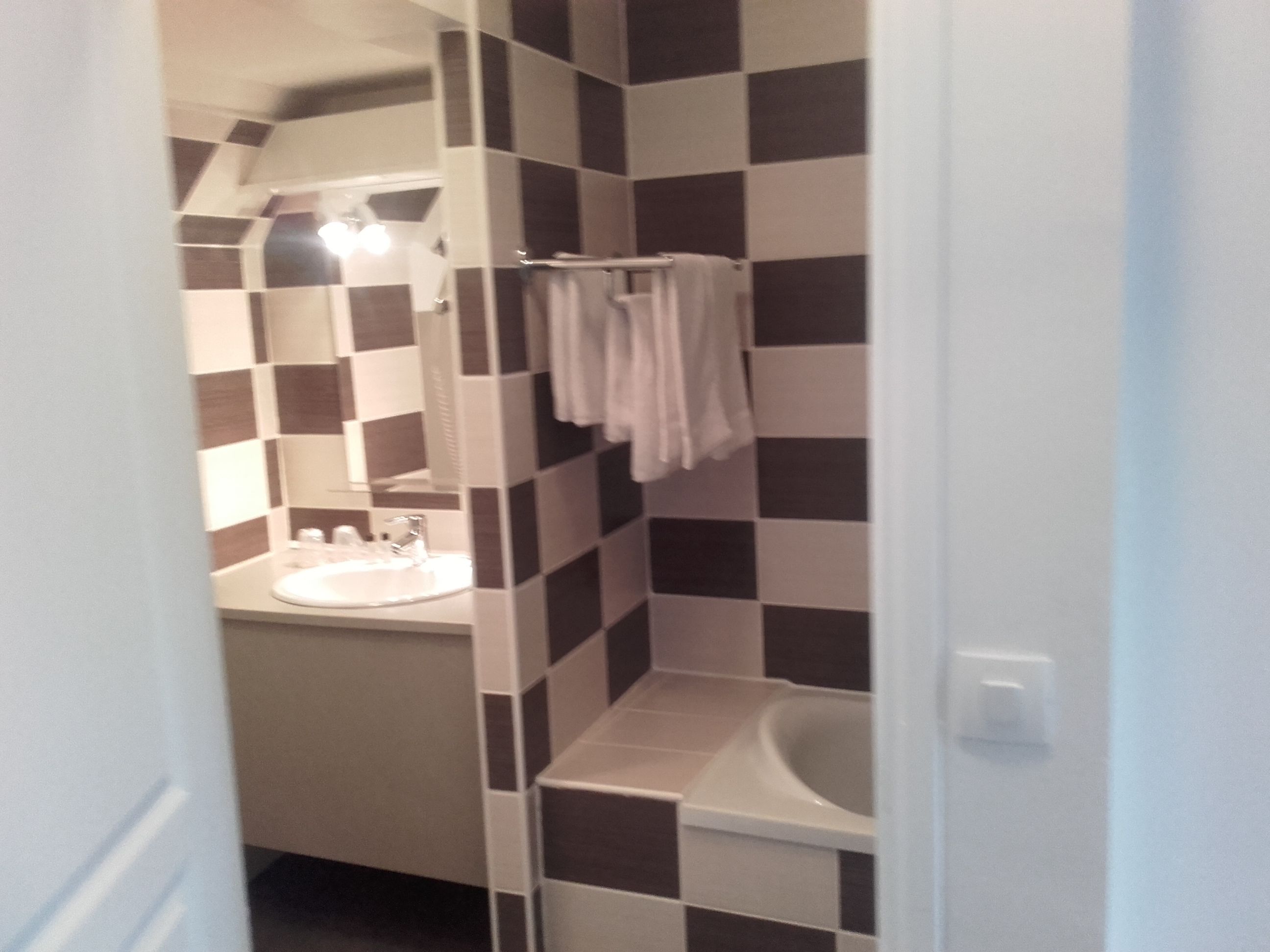 Un baño con piso de baldosas a cuadros, un lavamanos, un espejo y un perchero para toallas.
