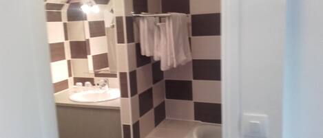 Un baño con piso de baldosas a cuadros, un lavamanos, un espejo y un perchero para toallas.