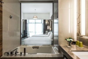 A modern hotel room with a large bed, a bathtub, and a bathroom with a sink and mirror.