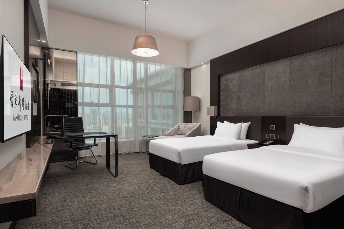 A hotel room with two beds, a desk, a chair, a lamp, and a large window.